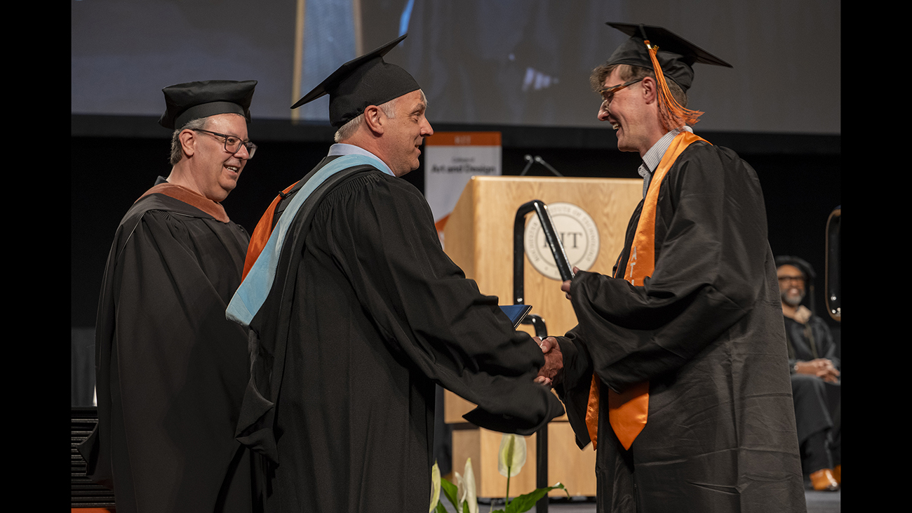 Faculty Ted Kinsman hands his son Parker his degree.