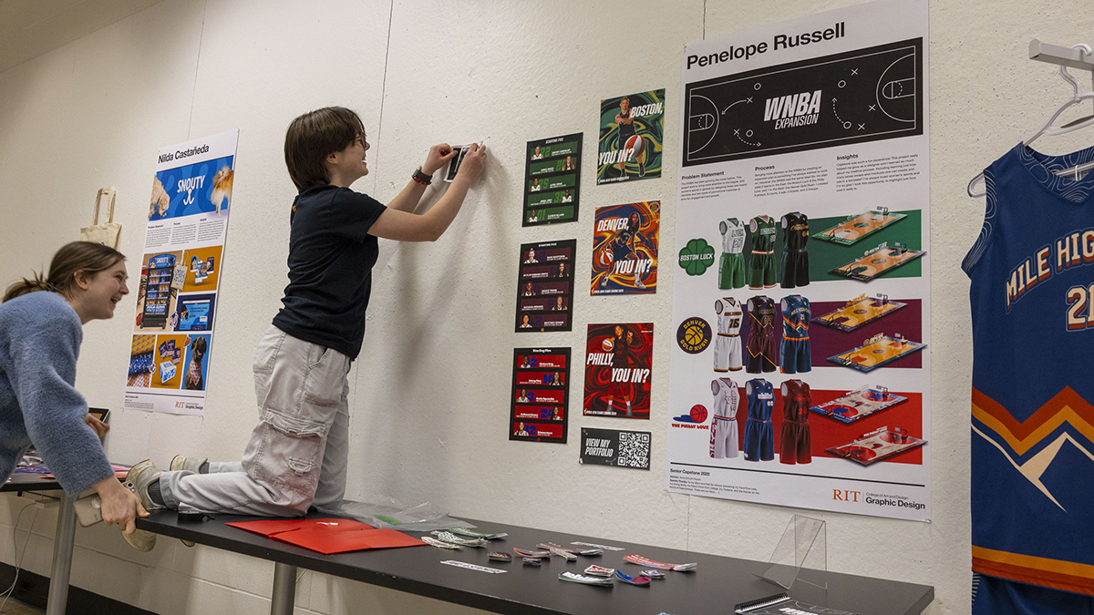 A student hags graphic design samples on a wall.