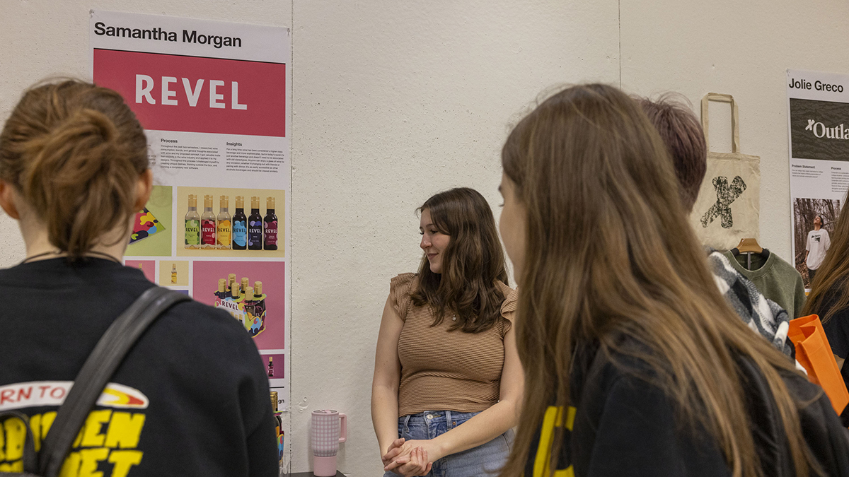A student presents their graphic design capstone, displayed on a poster.