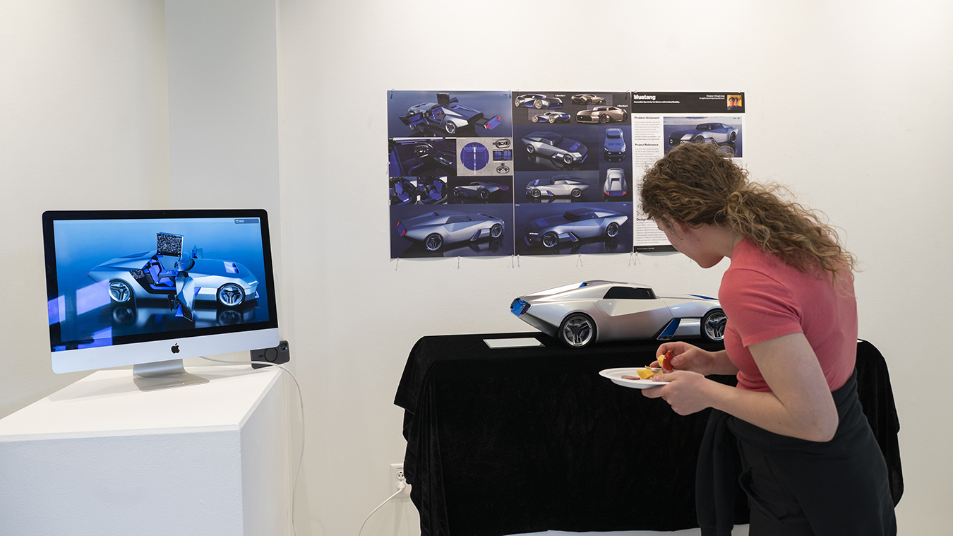 A gallery visitor looks at a 3D model of a futuristic-looking sports car.