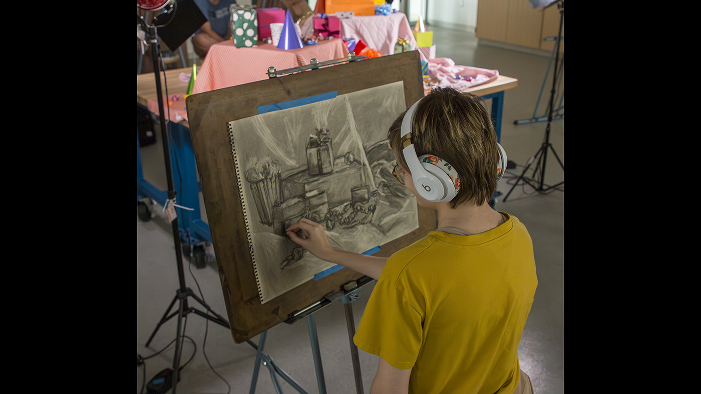 A student references a still life setup to recreate it as a drawing.