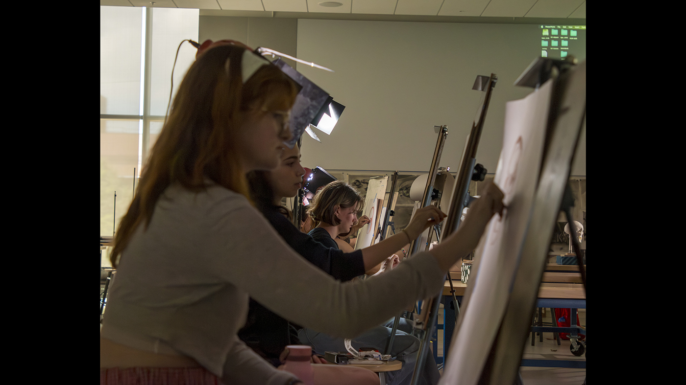 A group of high school students draw on easels.