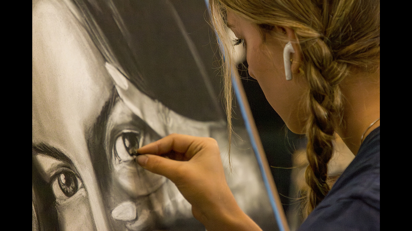A student draws a self-portrait using vine charcoal.