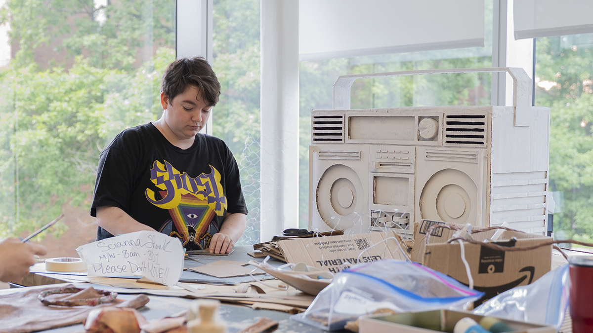 A student works on making a cardboard boombox in a studio space.