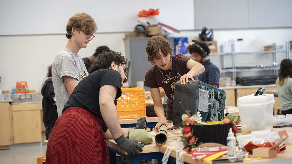 A group of students look at a wearable sculpture.