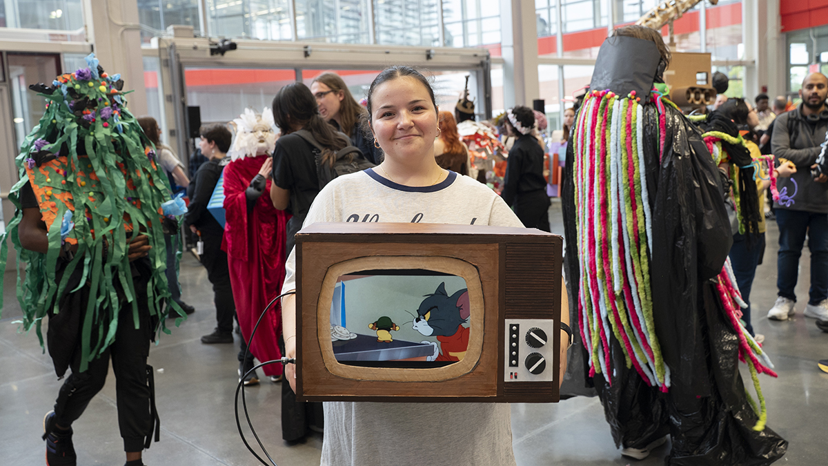 A student poses with a wearable TV playing a cartoon, Tom and Jerry.