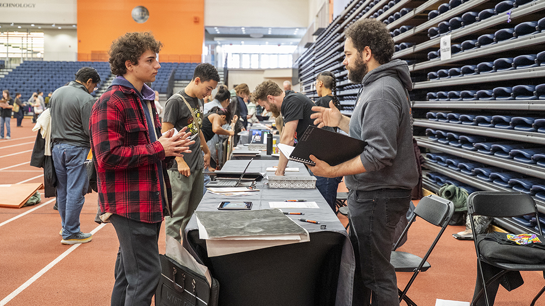 Faculty in a row reviewing student work in the Gordon Field House.