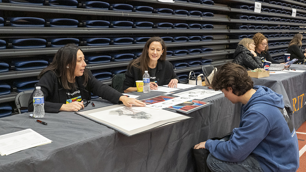 Faculty Marissa Tirone and Lori Resch speak with a student at a table.
