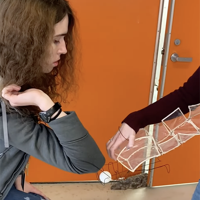 Students pass ping pong balls using wearable sculpture they designed.