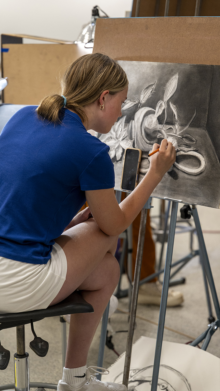A student draws a still life at an easel.
