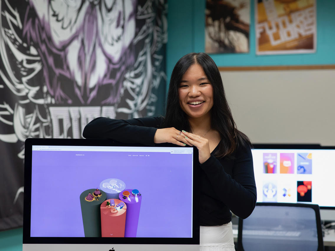Student Stephanie Liu poses behind a computer screen showcasing her work.