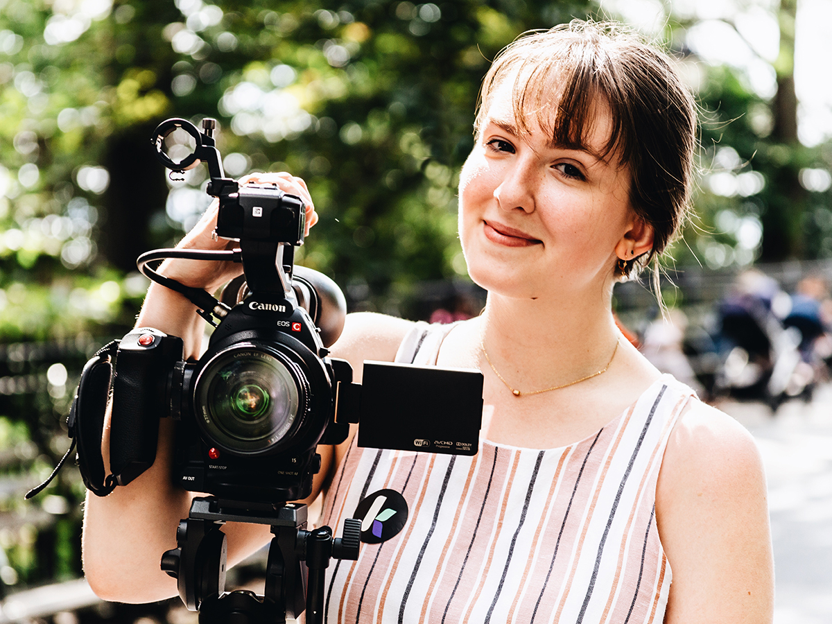 Trisha Pickelhaupt stands behind a camera on a tripod.