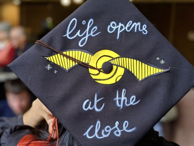 A decorated grad cap that reads "Life opens at the close."
