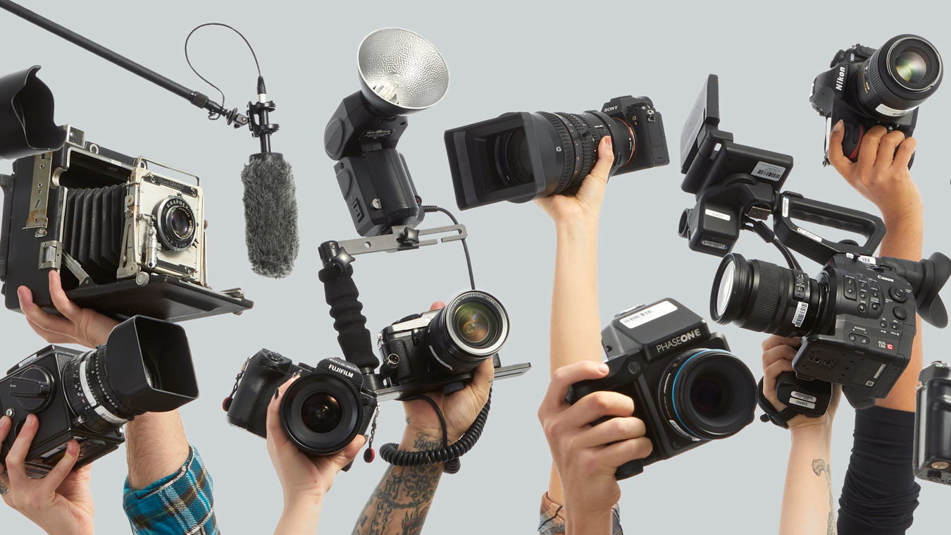 Multiple hands holding an array of professional cameras, including vintage and modern models, representing the School of Photographic Arts and Sciences.