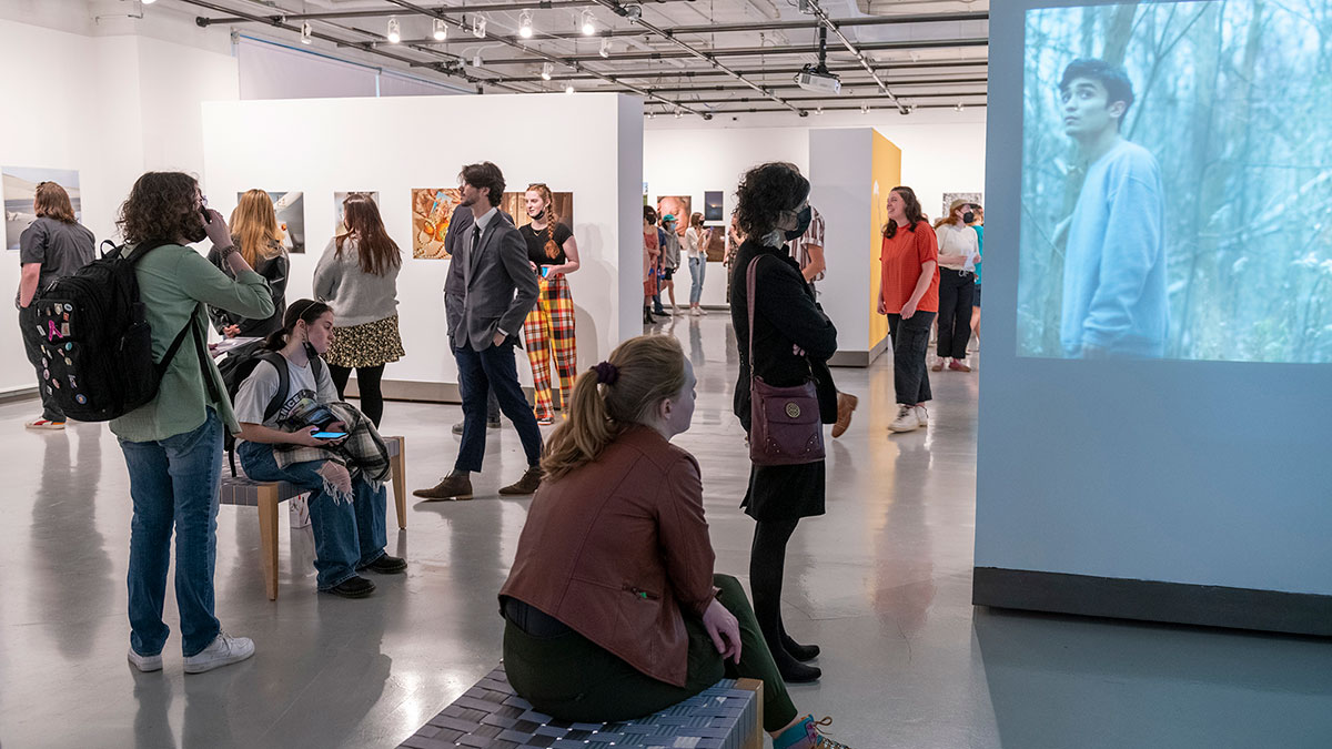 A group of people viewing artwork and video projections in a modern art gallery.