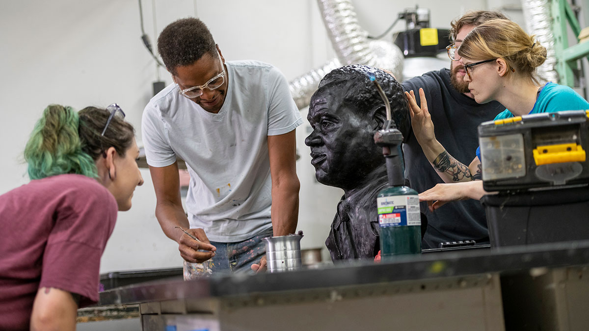 Four people collaborating on sculpting a large bust in a workshop setting.