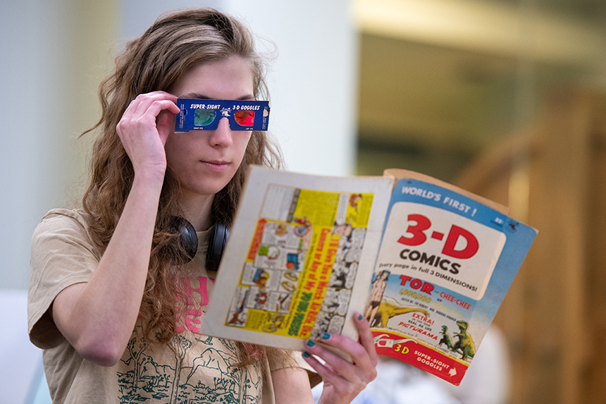 A student looks at a comic book using 3D glasses.