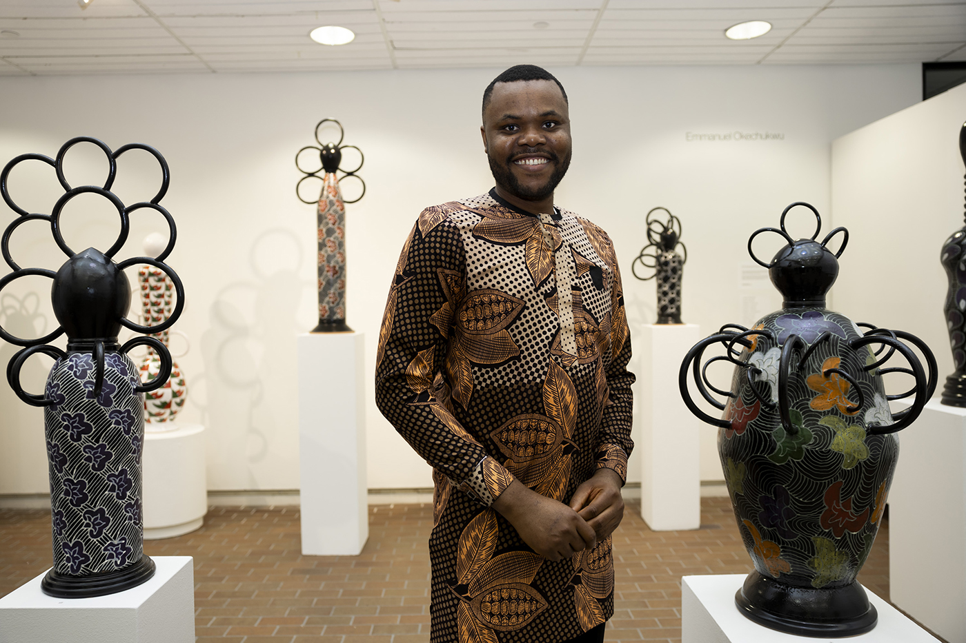 Emmanuel Okechukwu stands next to his ceramics sculptures in a gallery.