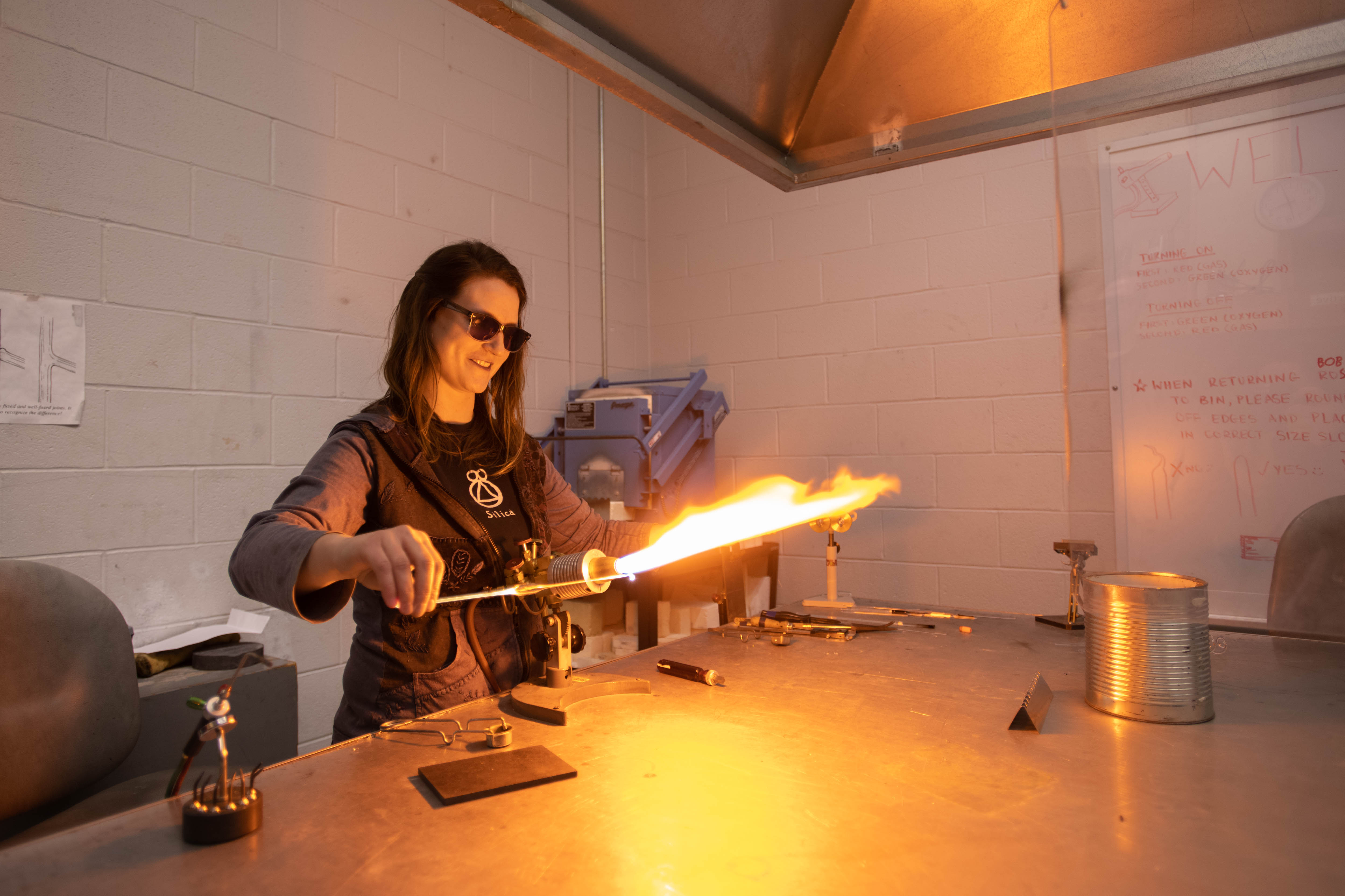 An MFA student works with a large flame to craft a glass object.