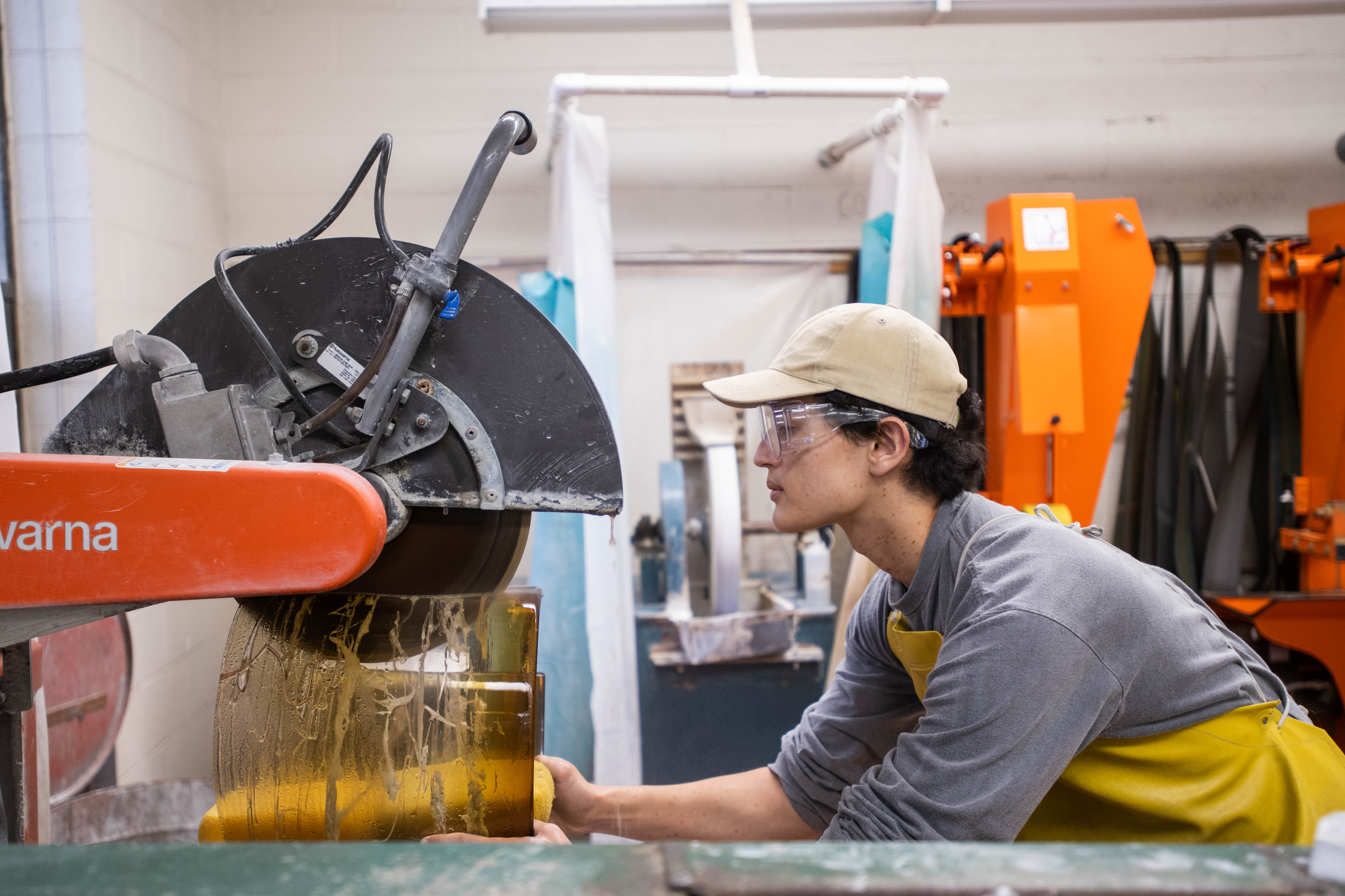 A student cuts a piece of glass on a saw in the cold shop.