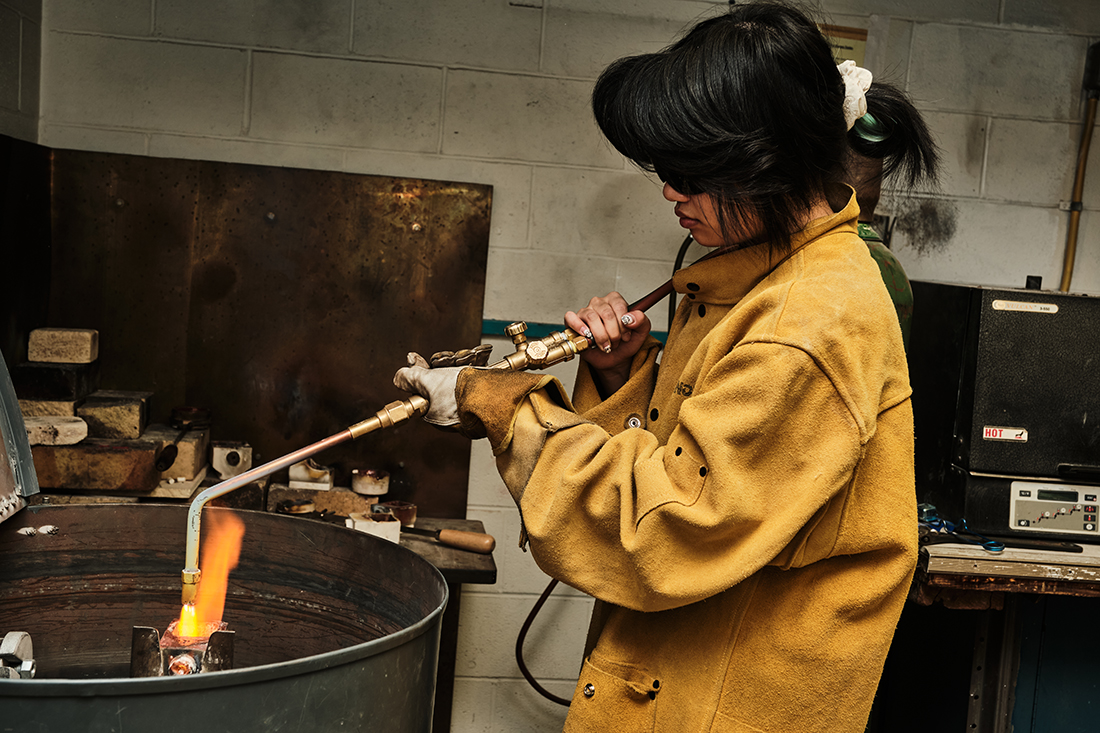 An RIT metals and jewelry design student works with a flame in the studio.