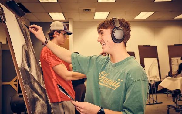 A smiling student draws at an easel.