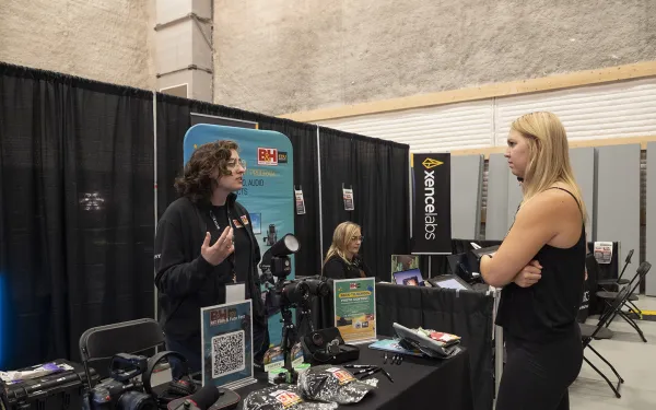 Conference attendees look at camera equipment on a table.