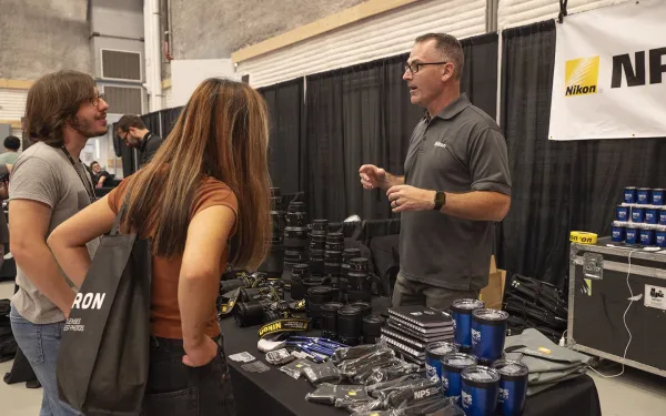Conference attendees look at camera equipment on a table.