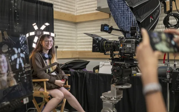 A conference attendee gets their photo taken while sitting in a director's chair.
