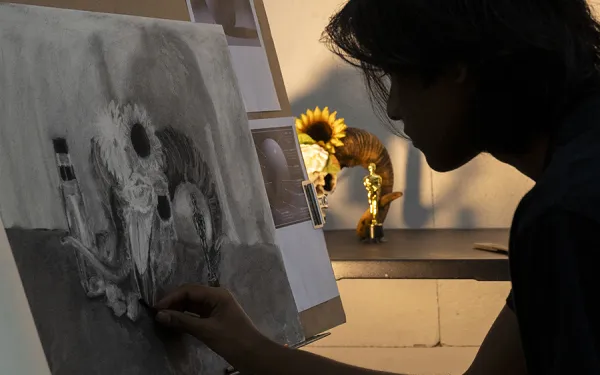 A shadowy artist draws at an easel.