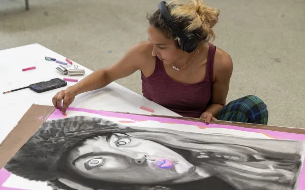 A student colors a pink background on a self-portrait.