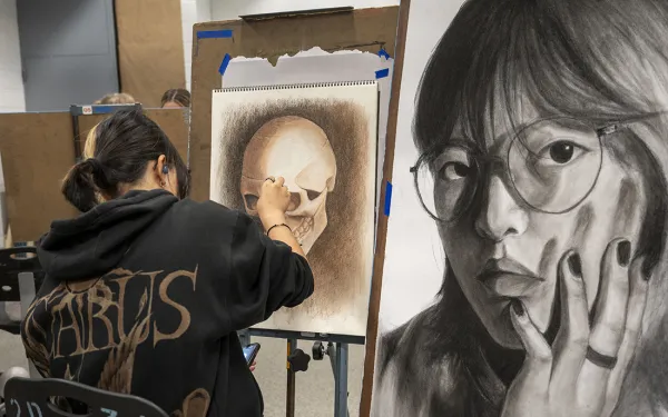 A student works next to their self portrait and skull drawings.