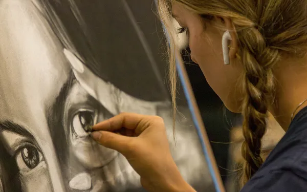 A closeup of a student drawing a self portrait.