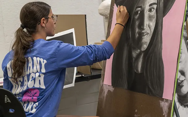 A student draws a self-portrait at an easel.