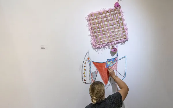 Faculty Taylor Kennedy installs a piece of her work on a gallery wall.