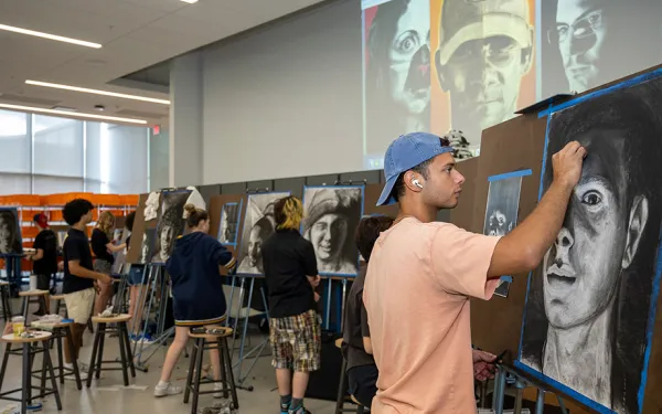 A classroom of students draw at easels.