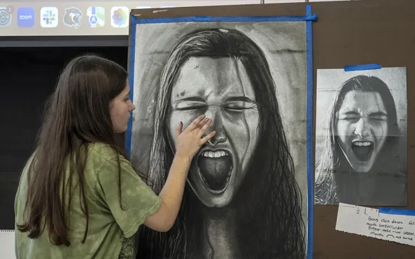 A student draws a self portrait at an easel.