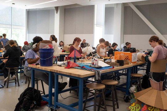 students build wearable cardboard pieces in a large workshop room.