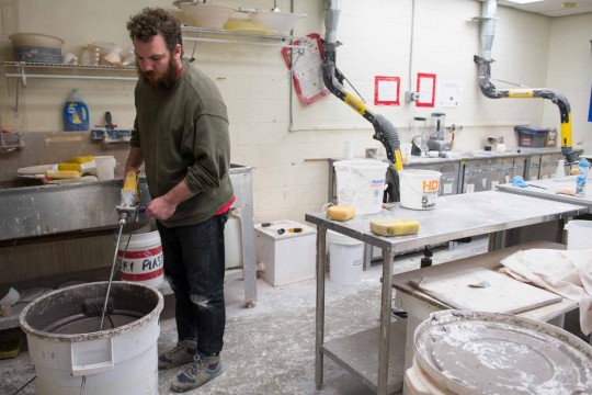 Student using a drill to mix in the clay and glaze formulation and spray booth room