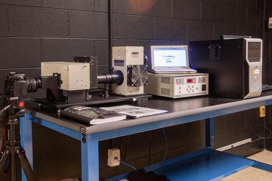 A piece of scientific lab equipment on a desk with a camera on the end.