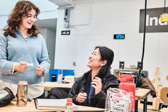 Two smiling students at a work station in the industrial design studio.
