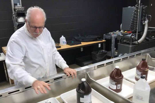 A man wearing a white coat looking at image development chemicals in a long sink with black walls in the background