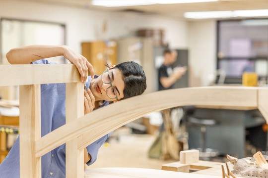 An RIT student uses a hand tool on a furniture piece.