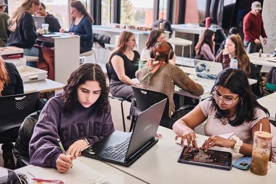 students work at tables in a large room.