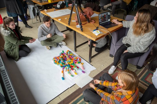 An overhead photo of students making a stop-motion video, with three students sitting on the floor with a pile of colorful paper slinkies.