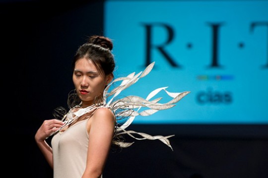 Person modeling jewelry necklace with large ribbon coming from the back on it, mimicking wings.