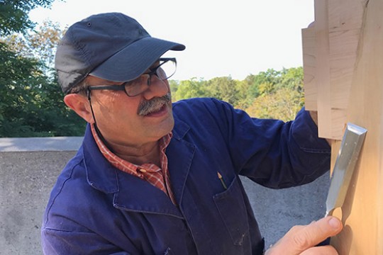 man scraping a piece of wood with a chisel.