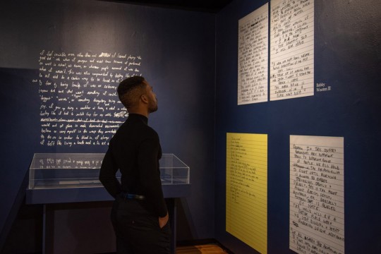 man looking at artwork of handwritten notes on gallery wall.