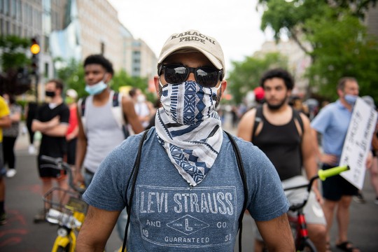 man wearing a baseball cap, sunglasses, and handkerchief over his face.