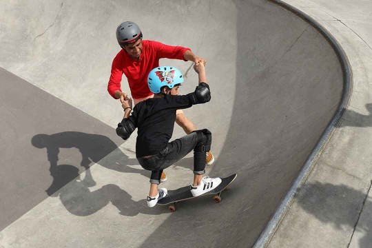 adult helping a kid to skateboard.